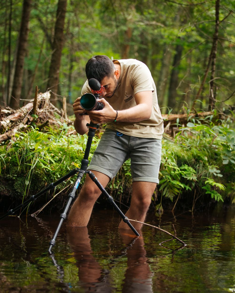 Omer standing in a forest creek, shooting on a tripod
