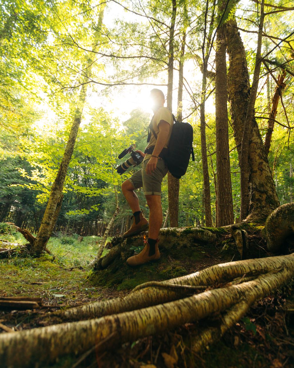 Omer in a sunlit forest with his camera and backpack