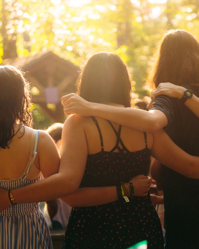 Three campers from behind, arms around each other in golden light